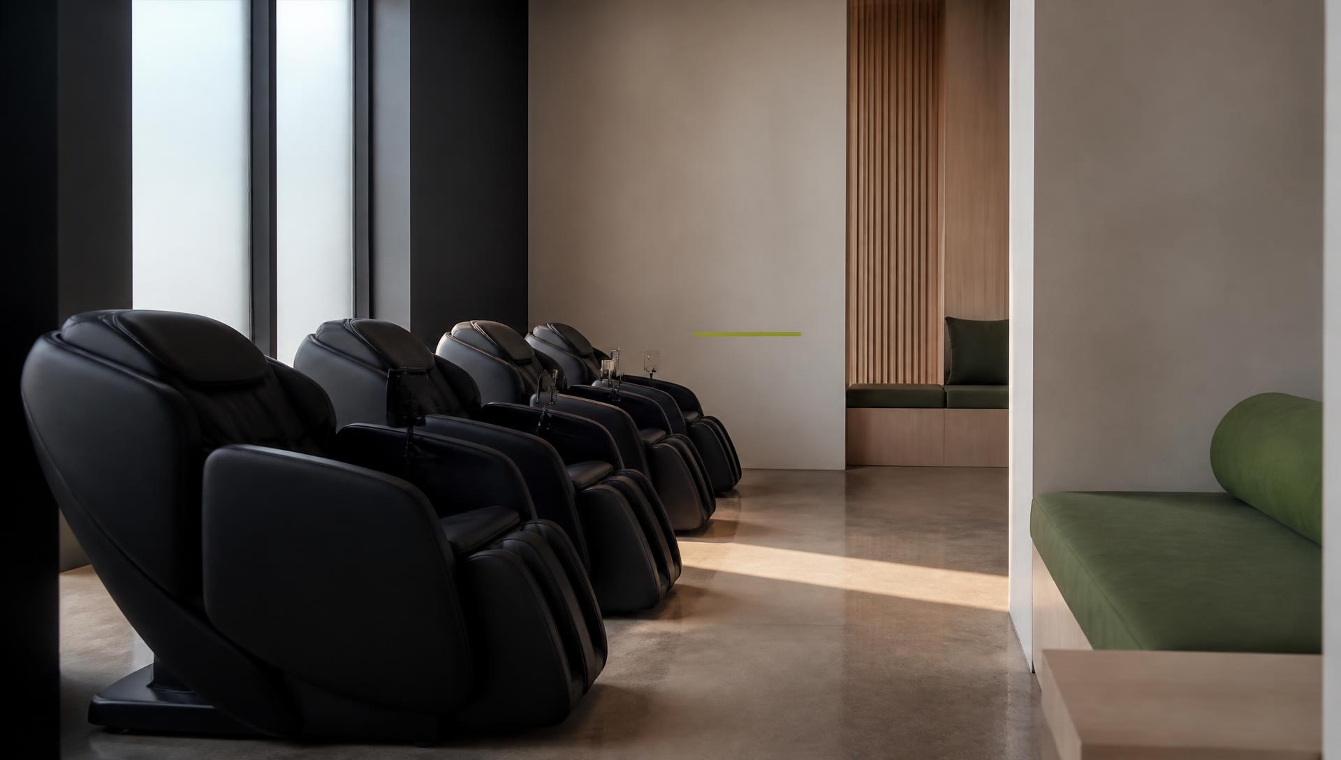 Recovery suite interior in soft daylight with matte black massage chairs, blond wood detailing, and concrete floor